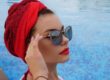 Femme avec un turban rouge porte des lunettes de soleil créateur au bord d'une piscine- tendance été 2026