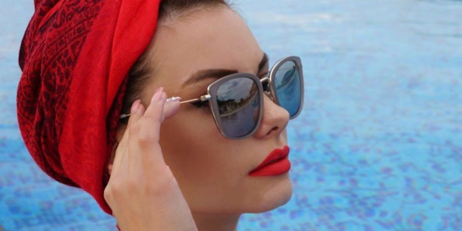 Femme avec un turban rouge porte des lunettes de soleil créateur au bord d'une piscine- tendance été 2026
