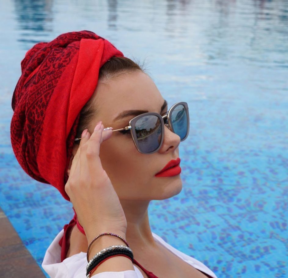 Femme avec un turban rouge porte des lunettes de soleil créateur au bord d'une piscine- tendance été 2026